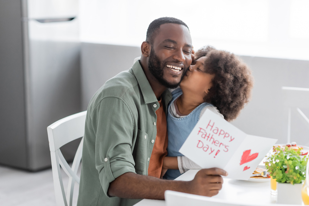 κατσαρομάλλη Αφροαμερικανή που φιλάει μάγουλο ευτυχισμένου πατέρα με ευχετήρια κάρτα την ημέρα των πατέρων  - Φωτογραφία, εικόνα