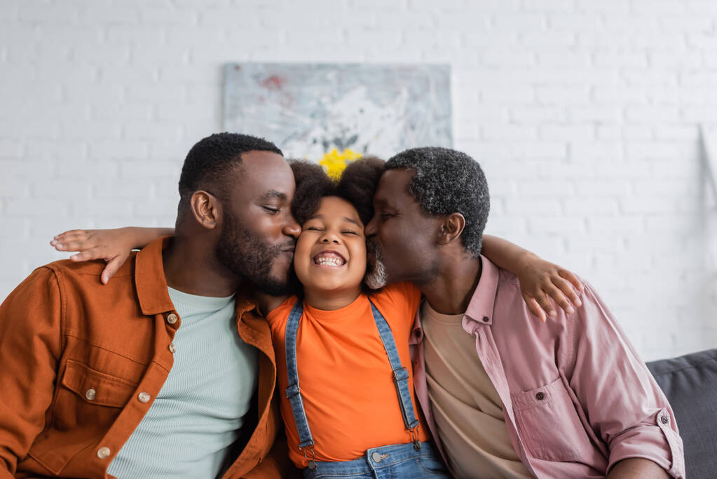 Αφρο-αμερικάνος πατέρας και παππούς φιλούν χαρούμενο παιδί στο σαλόνι  - Φωτογραφία, εικόνα
