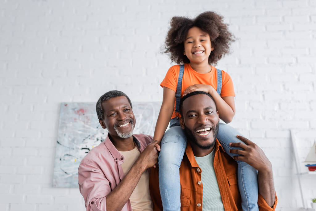 Aşırı neşeli Afrikalı Amerikalı çocuk evde baba ve büyükbabasıyla eğleniyor.  - Fotoğraf, Görsel