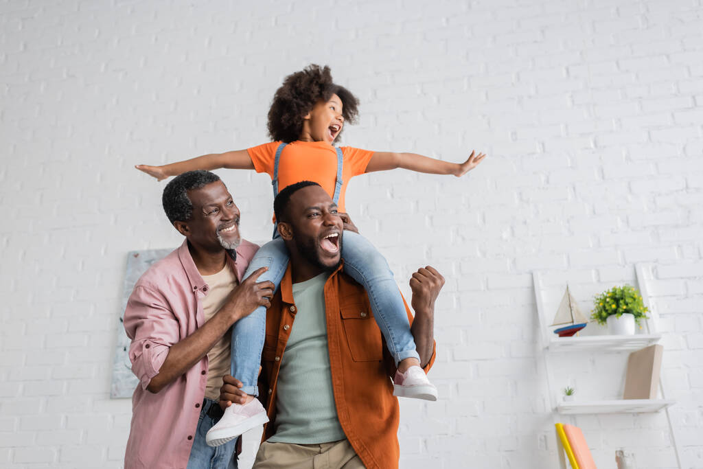 Emocionado hombre afroamericano divirtiéndose con su hija y su padre en casa  - Foto, imagen
