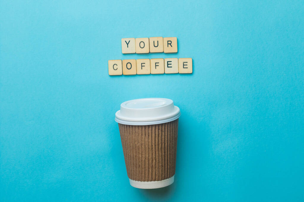 Une tasse de café en papier et un couvercle avec un panneau lisant votre café sur un fond bleu - Photo, image