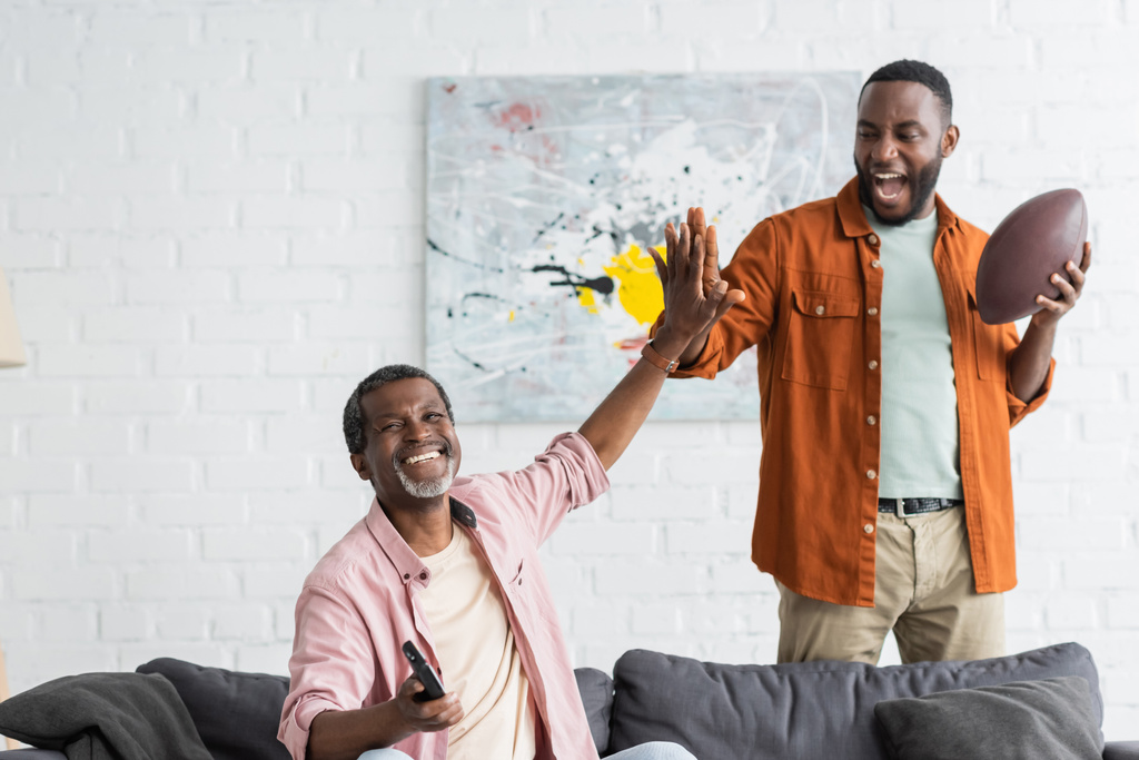Pozitív afro-amerikai apa és fia pacsit adnak, miközben otthon rögbi meccset néznek.  - Fotó, kép