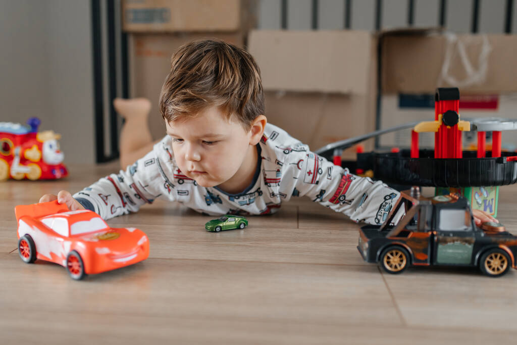 Niño feliz sentado en la alfombra blanca en casa y jugando con el juguete del coche. Foto de alta calidad - Foto, Imagen