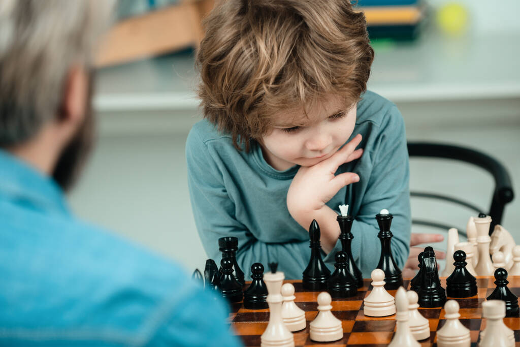 Отец учит сына играть в шахматы. Концепция образования и преподавания. Учитель и ребенок. Красивые отец и сын играют в шахматы, проводя время вместе
 - Фото, изображение