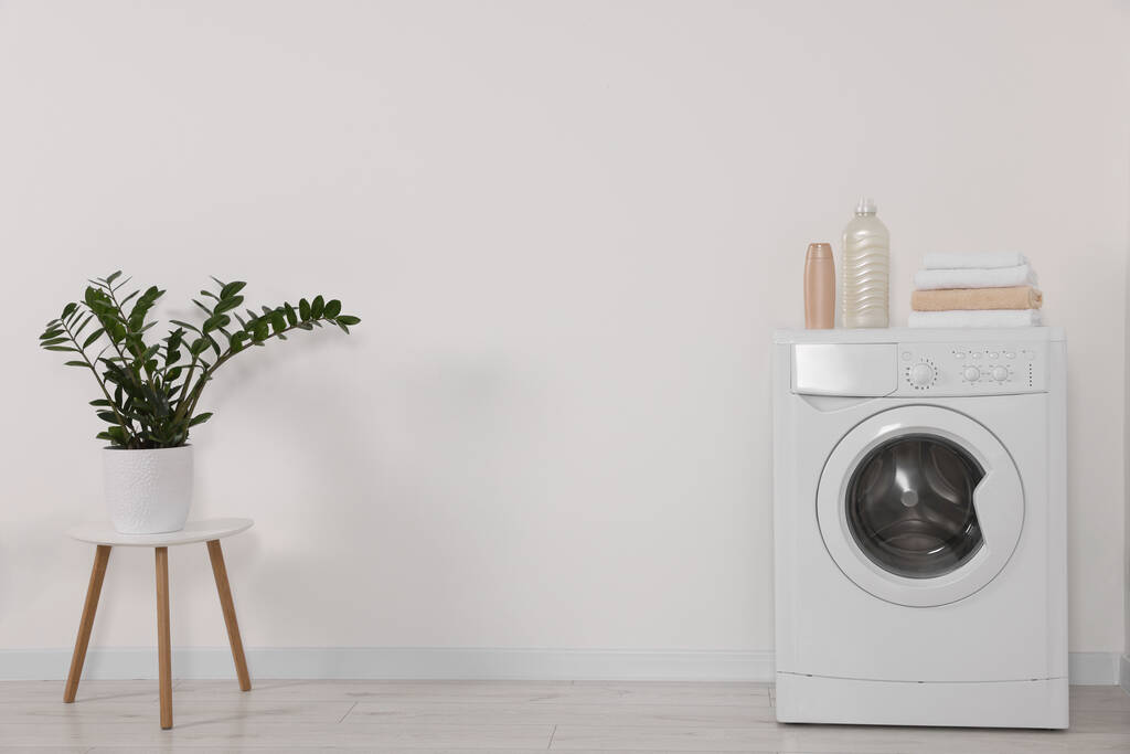 Современная стиральная машина и горшок растений на стуле против белой стены в помещении - Фото, изображение