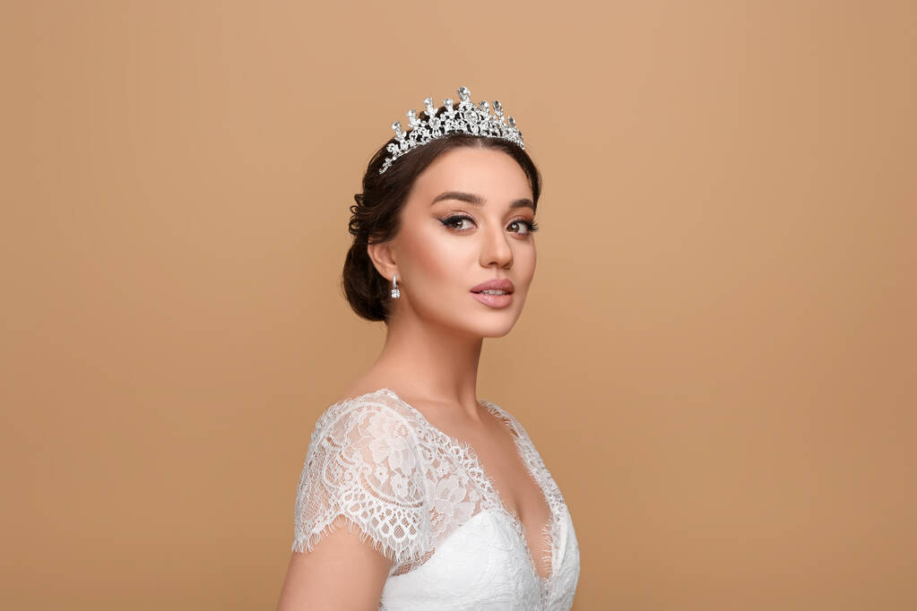 Gyönyörű fiatal nő visel luxus tiara bézs háttér - Fotó, kép