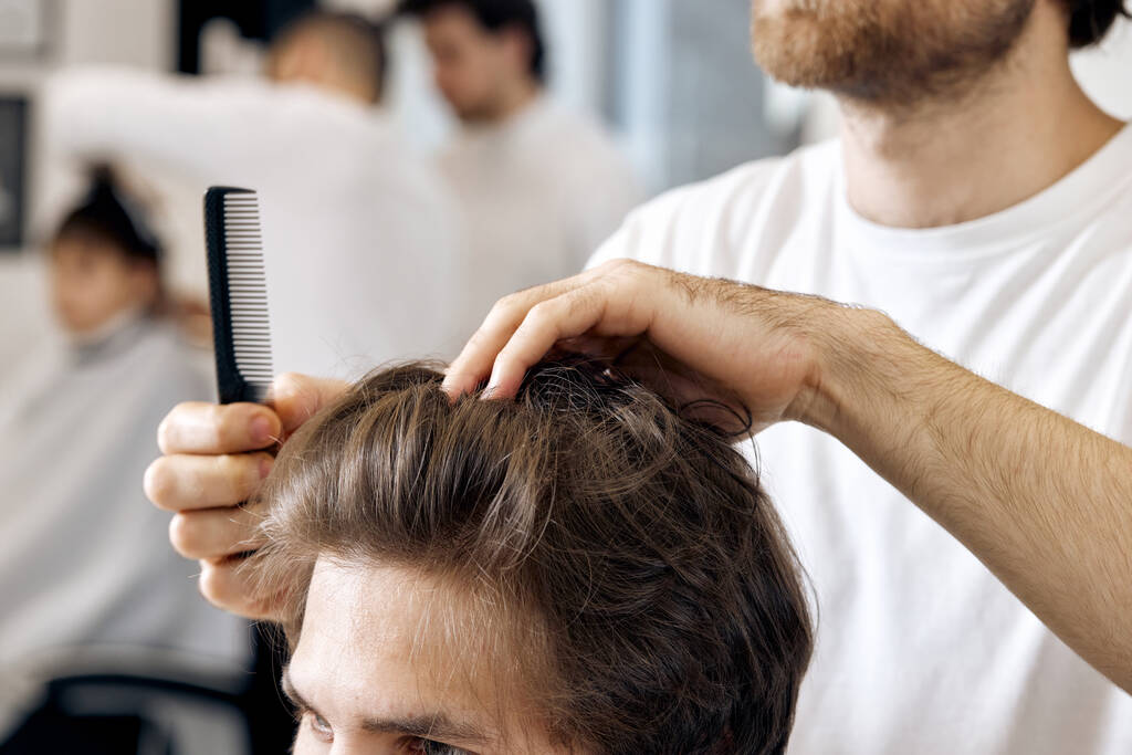 close-up, professional male hairstylist combing young customers hair in barbershop - Foto, Imagem