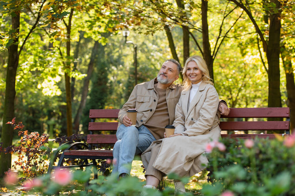 Una coppia matura felicissima che tiene in mano il caffè mentre trascorre del tempo nel parco  - Foto, immagini