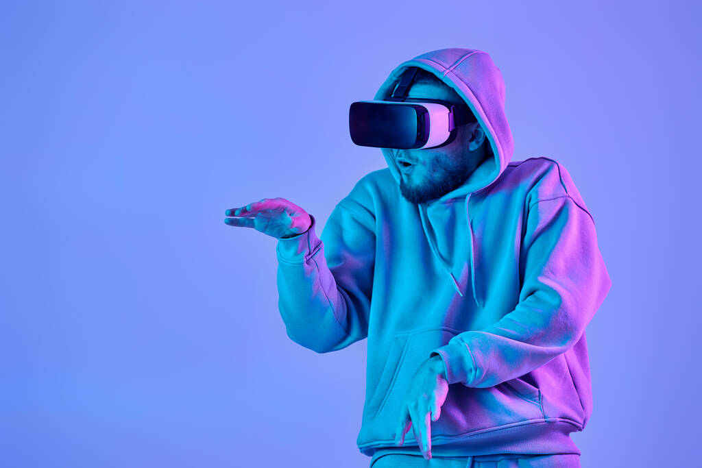 mies huppari käyttäen virtuaalitodellisuus lasit ja pelaa videopelejä sinisellä pohjalla. Neonvalot - Valokuva, kuva