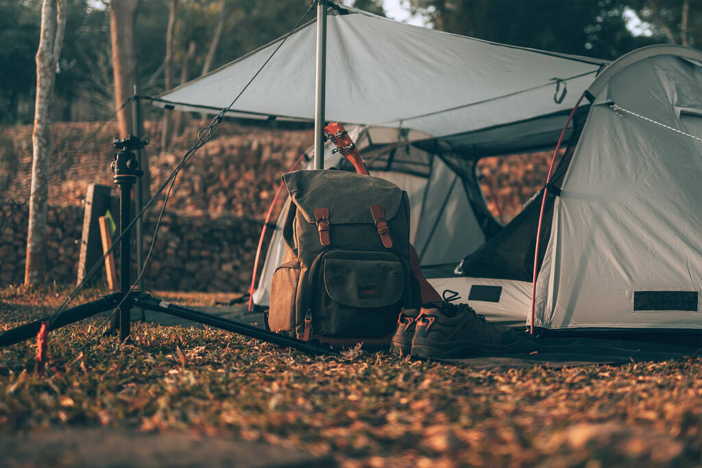 Attrezzature da campeggio, borse, scarpe, ukulele, treppiede accanto alla tenda al mattino. Campo oggetti, concetto di viaggio e vocazione. - Foto, immagini