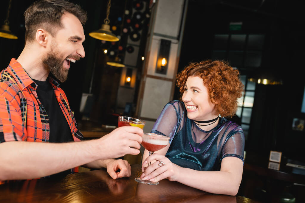Lächelnde Freunde klappern kalte Cocktails in der Nähe des Holzstandes in der Bar  - Foto, Bild