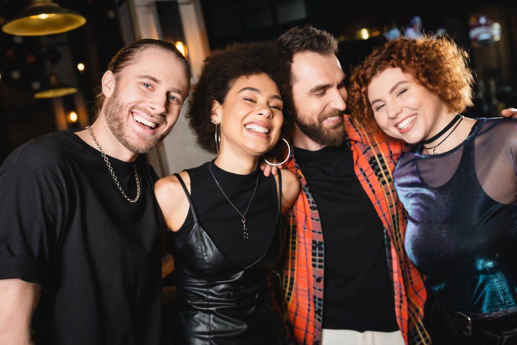 Bearded man hugging multiethnic friends and smiling at camera in bar  - Photo, Image