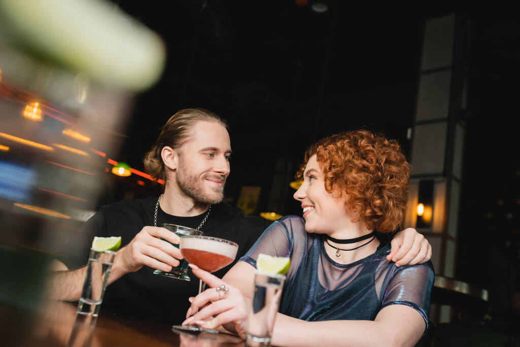 Positieve man knuffelen rood harige vriend met cocktail in de buurt staan in bar  - Foto, afbeelding