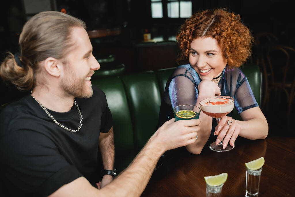 Vidám vörös hajú nő kezében lóhere klub koktél közel barát és állni a bárban  - Fotó, kép
