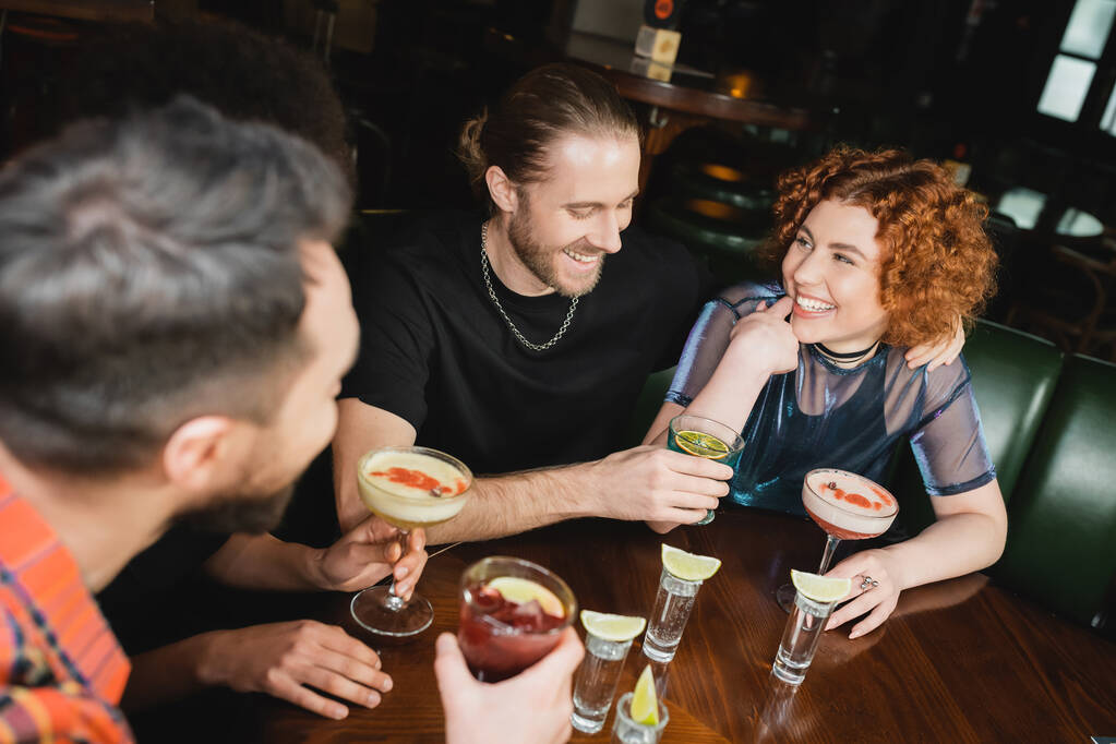 Un homme souriant tenant un cocktail lagon bleu près d'amis multiethniques passe du temps dans un bar  - Photo, image