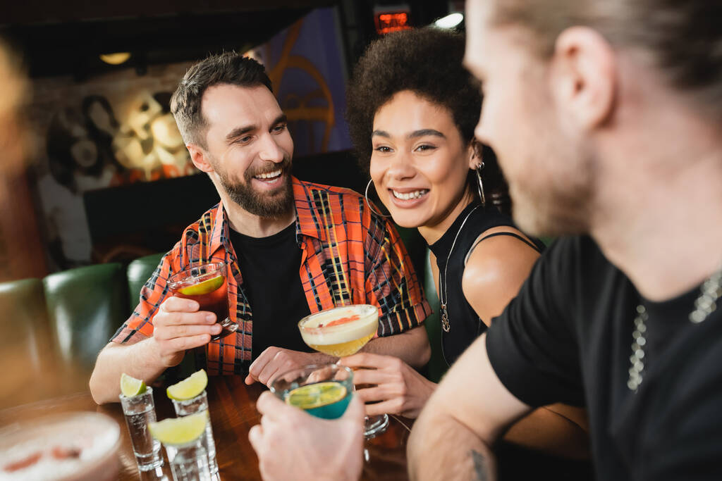 Веселі міжрасові друзі розмовляють біля коктейлів і текіли зі свіжим лаймом в барі
  - Фото, зображення