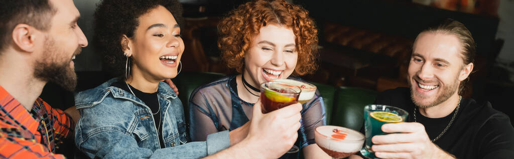 Позитивные мультиэтнические люди, держащие разные коктейли во время звонка в баре, баннере  - Фото, изображение
