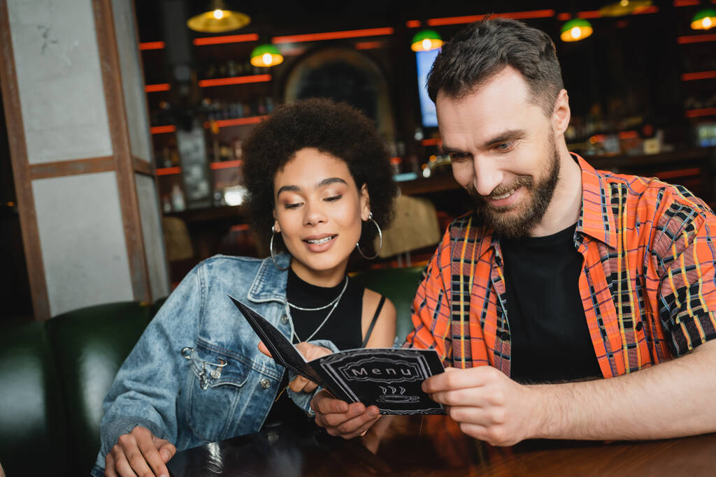 Veselí multietničtí přátelé v neformální oblečení při pohledu na menu v baru ve večerních hodinách  - Fotografie, Obrázek