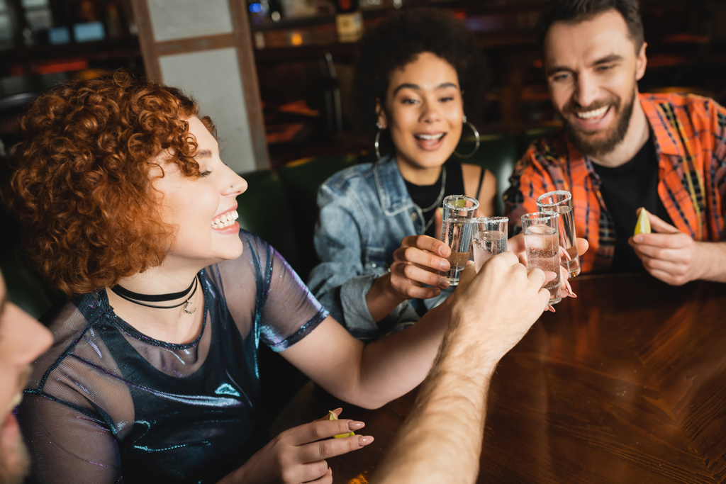 Amigos multiétnicos positivos sosteniendo tiros de tequila con sal y lima en el bar  - Foto, imagen