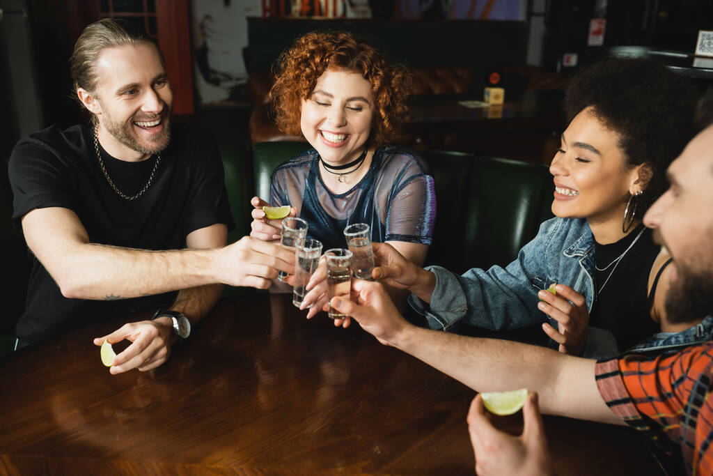 Unbekümmerte multiethnische Freunde klappern Tequila und halten nachts Limetten in der Bar  - Foto, Bild