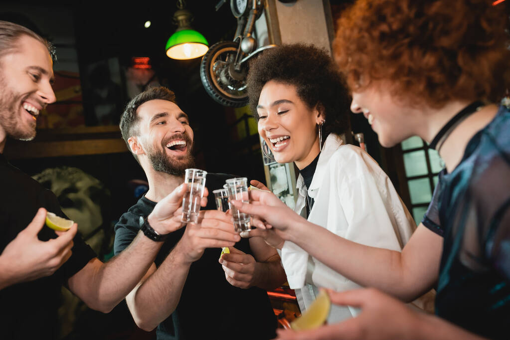 Positieve man klinkende tequila met interraciale vrienden terwijl het doorbrengen van tijd in bar  - Foto, afbeelding