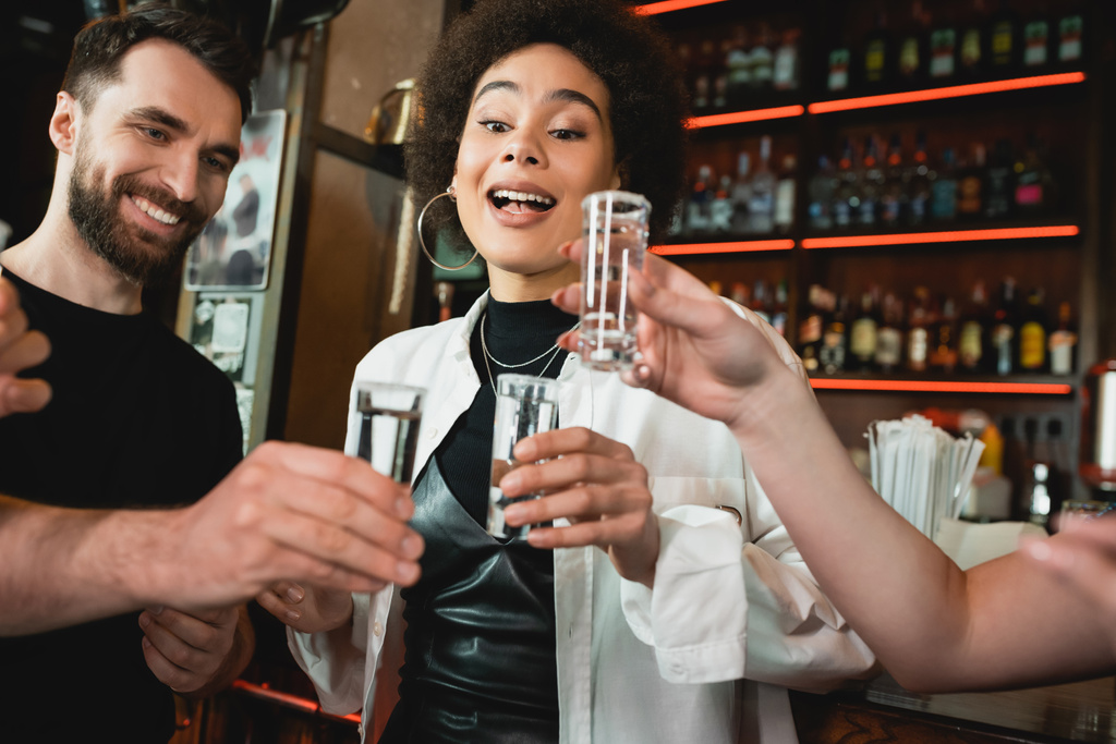 Excitada afro-americana segurando tequila tiro com sal perto de amigos no bar  - Foto, Imagem