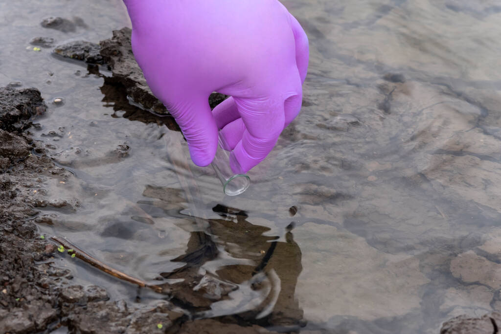 Vesinäyte joesta. Käsi hanskassa kerää vettä koeputkessa. ekologinen käsite - Valokuva, kuva