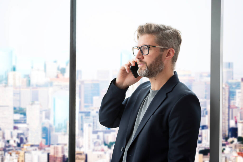 Důvěryhodný obchodník, který používá smartphone a má hovor, když stojí v kanceláři. Profesionální muž v obleku a brýlích. - Fotografie, Obrázek