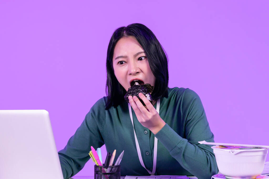 concepto de trabajo de negocios, joven mujer asiática coreana concentrándose en su trabajo mientras come fideos taza y kimbap triangular - Foto, imagen