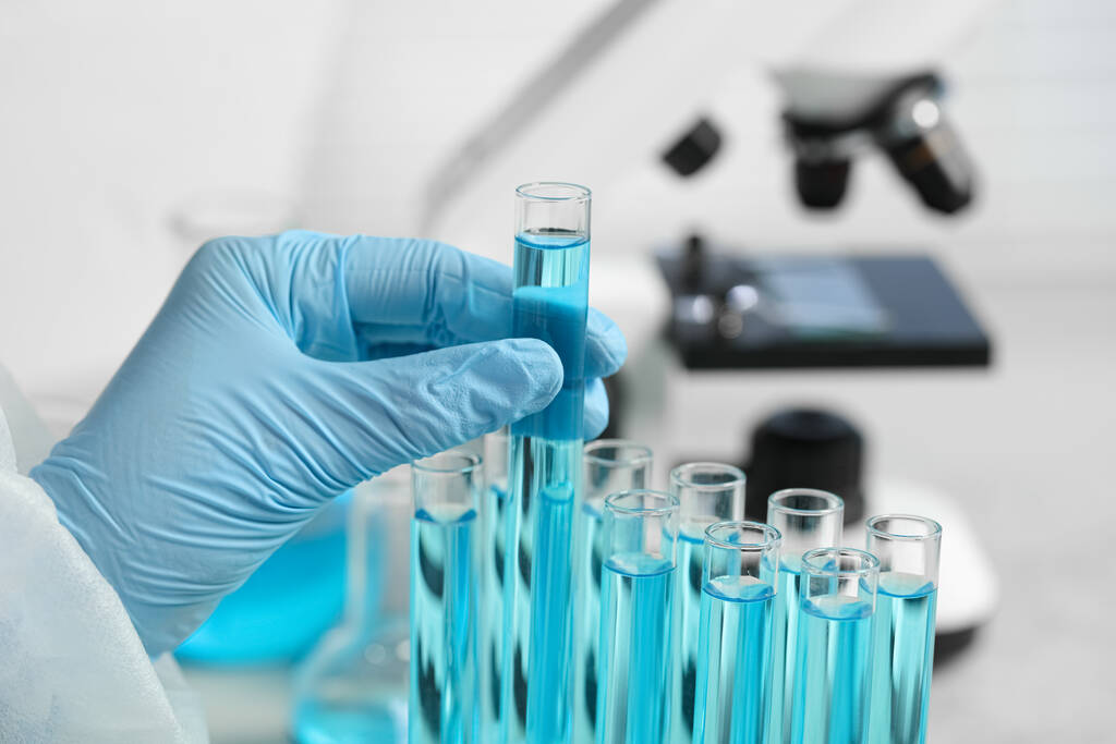 Scientist taking test tube with light blue liquid in laboratory, closeup - Valokuva, kuva
