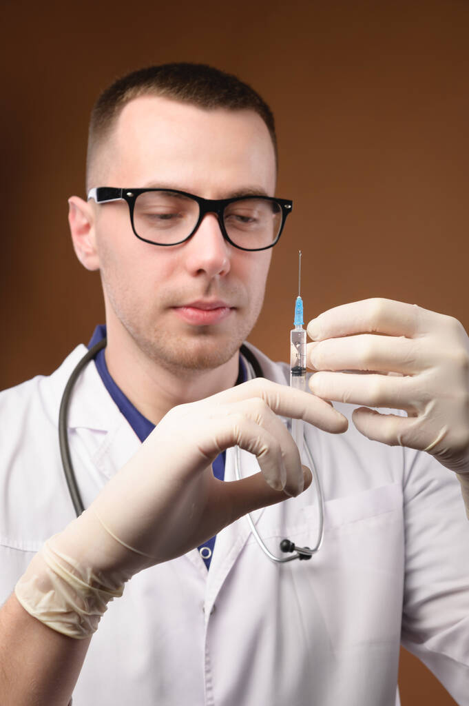 Caucasian male doctor holding a syringe in his hands in uniform, studio shot. - Foto, Imagen