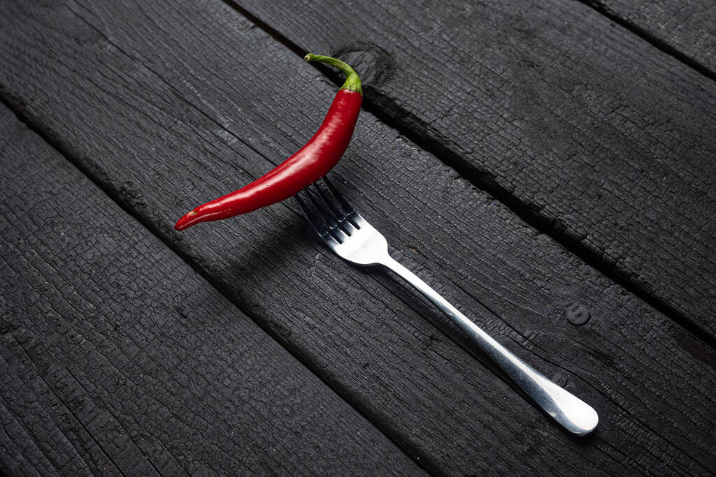 Ένα κόκκινο πιπέρι τσίλι σε ένα πιρούνι σε ένα μαύρο τραπέζι. - Φωτογραφία, εικόνα