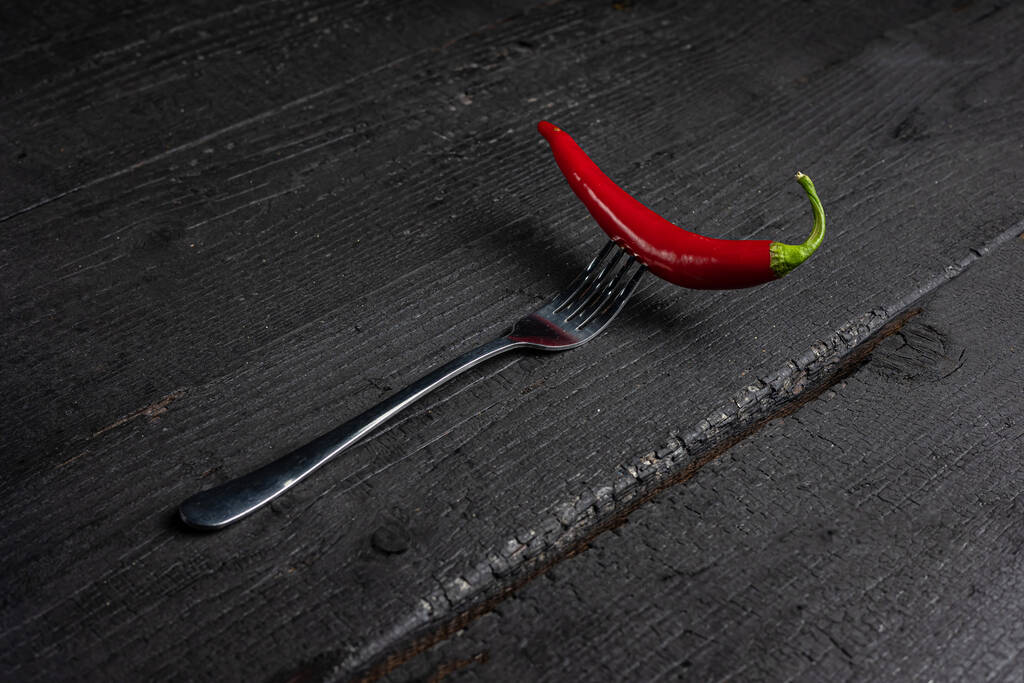 Un chile rojo en un tenedor sobre una mesa negra. - Foto, Imagen