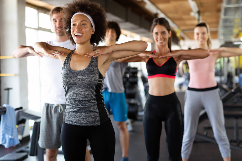 Gruppe junger fitter Menschen, Freunde, die lächeln und Sport im Fitnessstudio treiben. Menschen bewegen sich, erarbeiten Konzept. - Foto, Bild