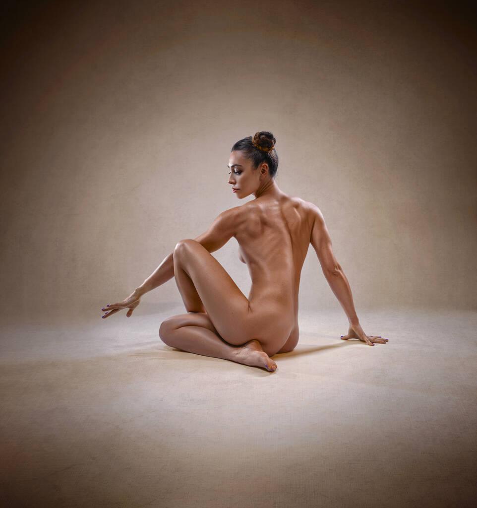 Menina de fitness sexy bonita com uma grande figura de aptidão muscular flexionando seu corpo perfeito em uma pose de ioga criativa no estúdio. - Foto, Imagem