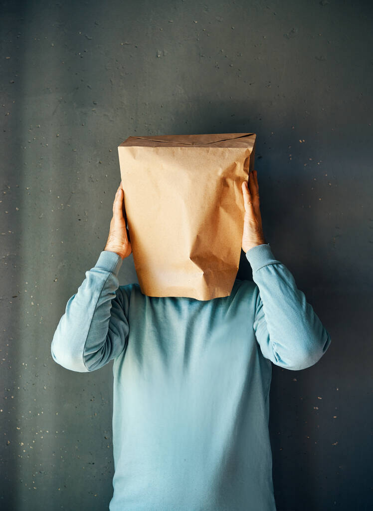 Upset man with a paper bag on head touching temples, suffering from strong tension headache over gray background. Emotion concept - Photo, Image