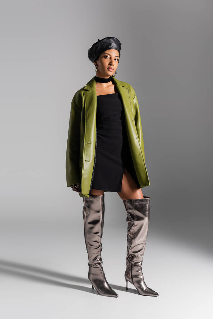 ブーツとグレーの背景に革のコートでスタイリッシュなアフリカ系アメリカ人モデルの完全な長さ - 写真・画像