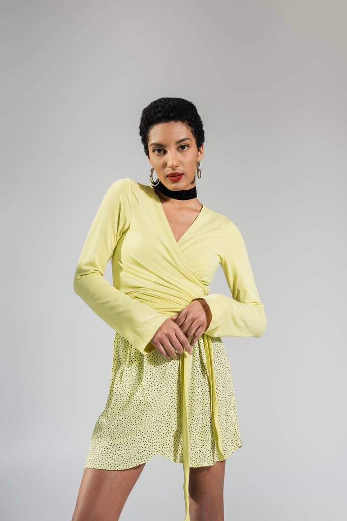 graziosa giovane modella afroamericana in abiti gialli in piedi isolata sul grigio  - Foto, immagini