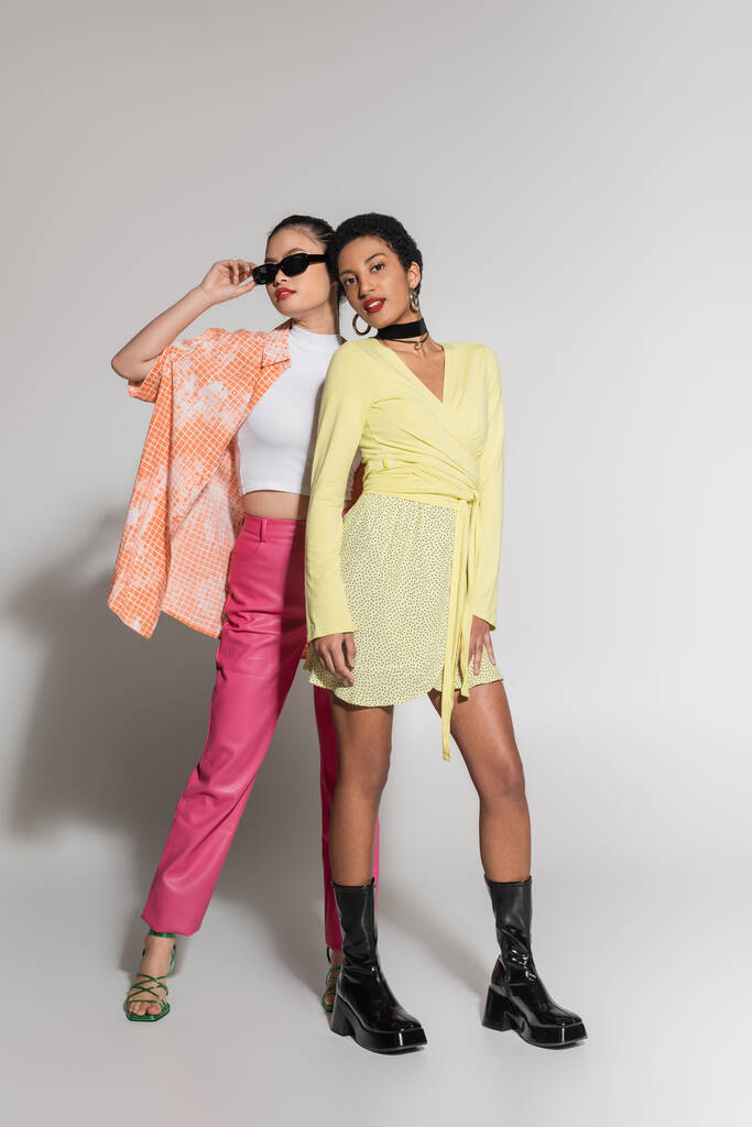 Πλήρες μήκος της μόδας διαφυλετικά μοντέλα σε πολύχρωμα ρούχα στέκεται σε γκρι φόντο  - Φωτογραφία, εικόνα