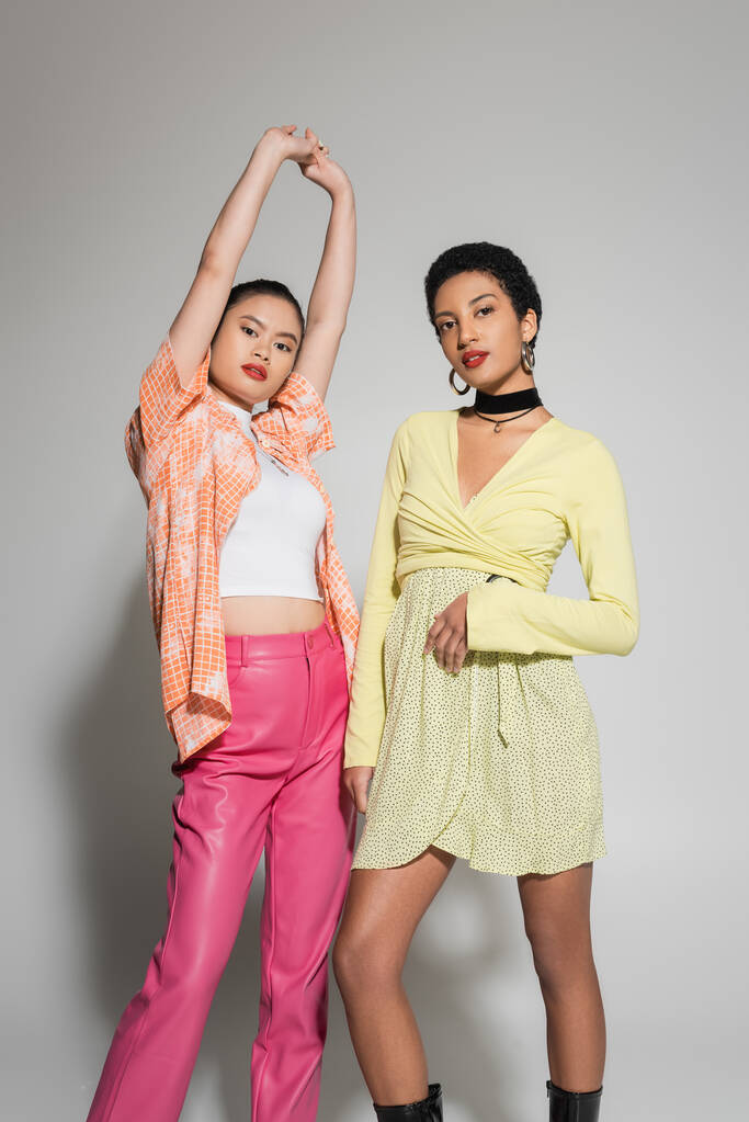 Modelos multiétnicos elegantes em roupa brilhante posando em fundo cinza  - Foto, Imagem