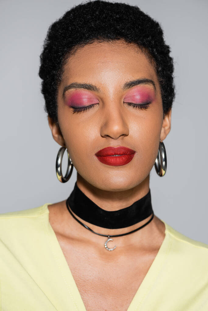 Portrét africké americké ženy s barevným make-upem zavírající oči izolované na šedé  - Fotografie, Obrázek