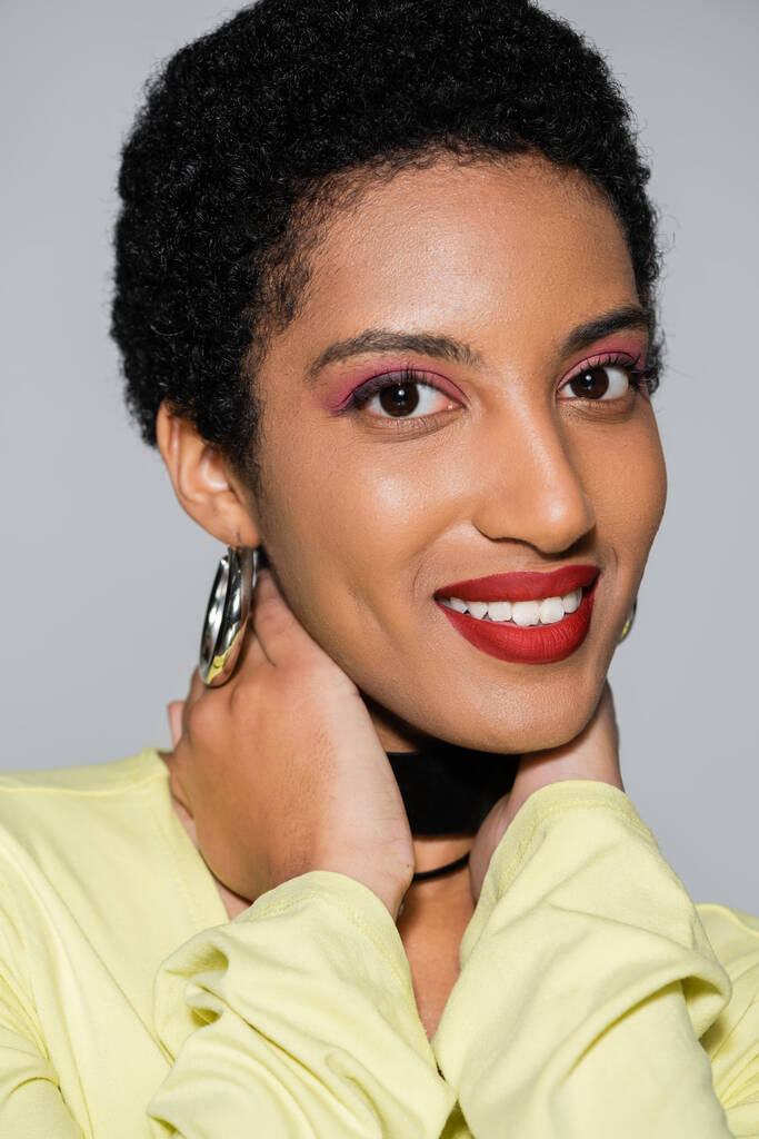 Unbekümmerte Afroamerikanerin mit Make-up am Hals isoliert auf grau  - Foto, Bild