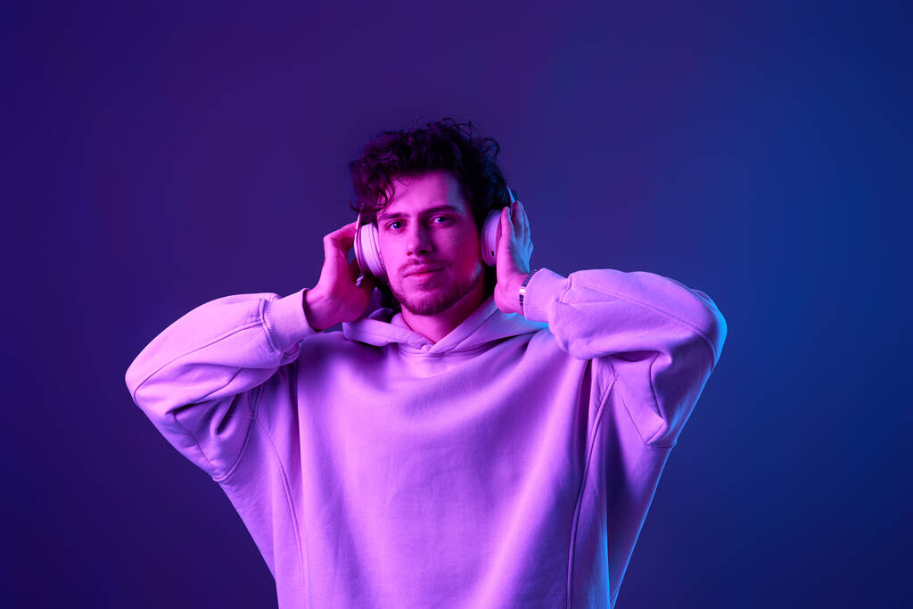 handsome man listening to music with wireless headphones on blue background. Neon lighting - 写真・画像