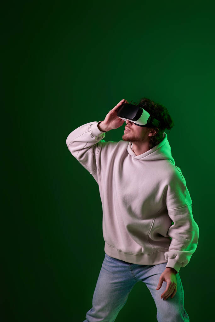 man in sweatshirt using virtual reality headset on green background. Neon lighting - Foto, Bild