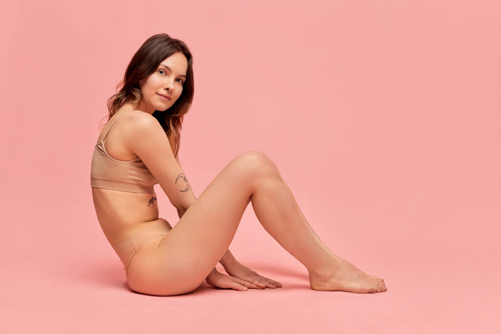 Portrait of young, beautiful, slim girl in beige underwear posing against pink studio background. Self-care and acceptance. Concept of body and skin care, figure, fitness, health, wellness. - Photo, Image