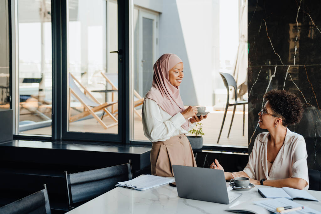 Bizneswoman w średnim wieku i jej koleżanka muzułmanka pracująca razem w biurze - Zdjęcie, obraz