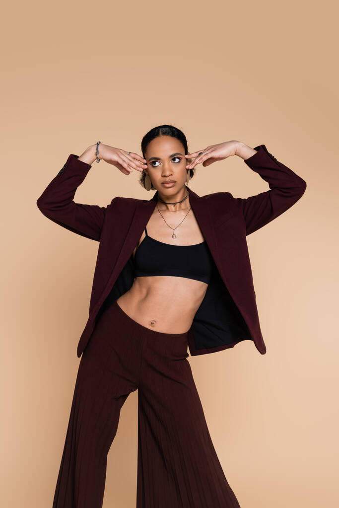 young african american woman in crop top and stylish maroon blazer posing isolated on beige  - Photo, Image