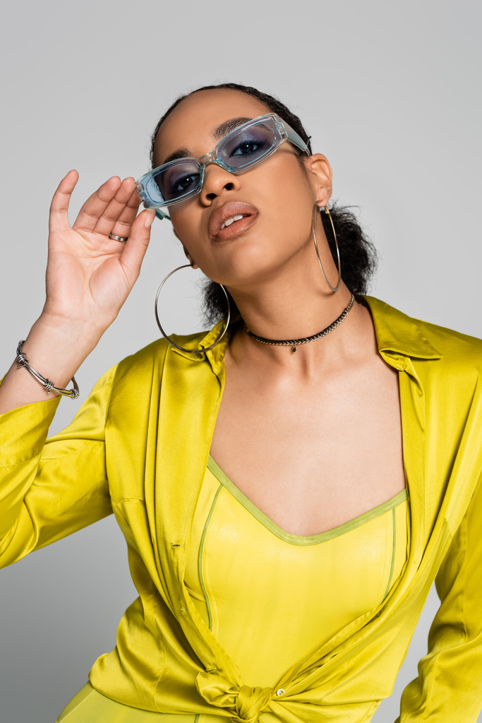 stylowa Afroamerykanka ubrana w modne niebieskie okulary przeciwsłoneczne na szaro  - Zdjęcie, obraz