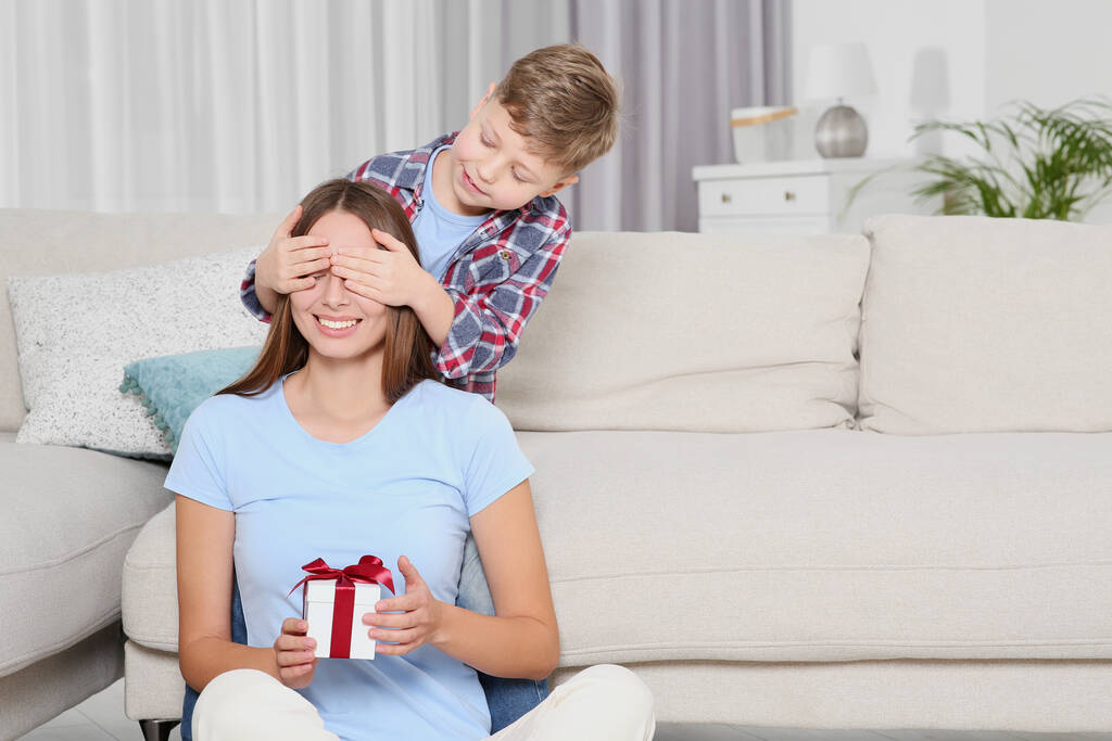 Pequeño niño presentando a su madre con regalo en el sofá en casa - Foto, Imagen