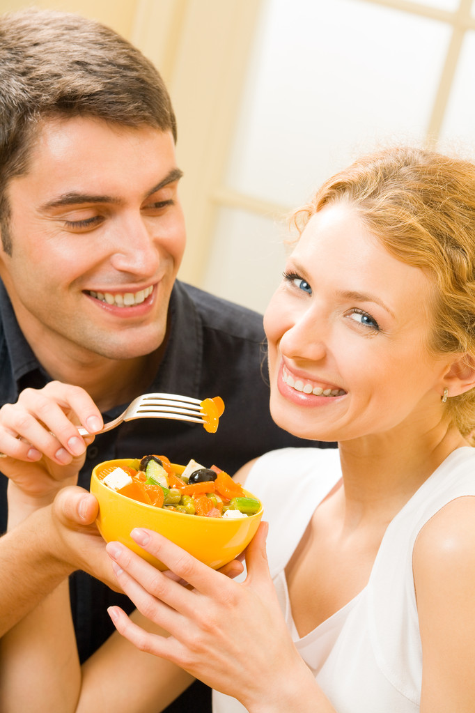 Jovem casal feliz comendo salada em casa juntos
 - Foto, Imagem
